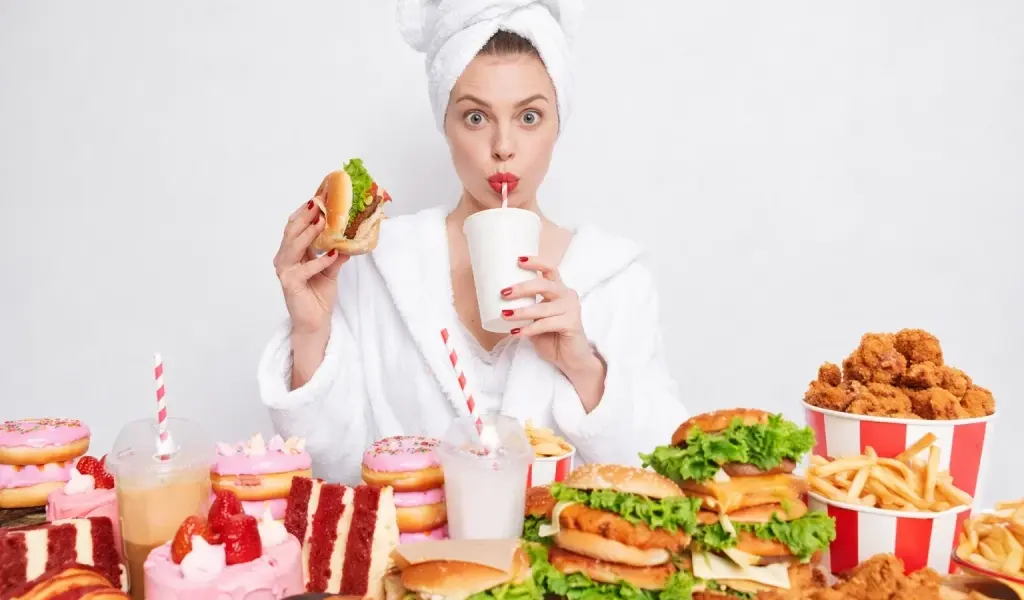 Mujer rodeada de hamburguesas, fritos, refrescos y dulces como ejemplo de la baja calidad alimentaria en Espa&ntilde;a