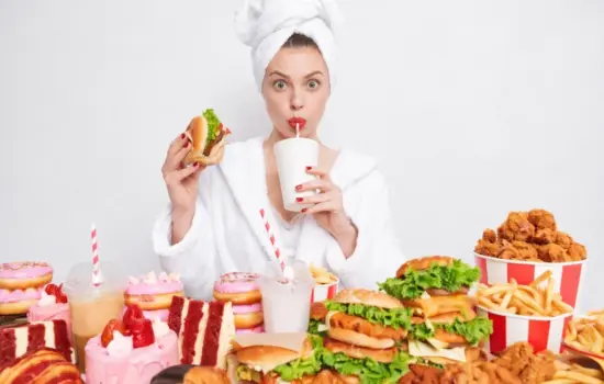 Mujer rodeada de hamburguesas, fritos, refrescos y dulces como ejemplo de la baja calidad alimentaria en España