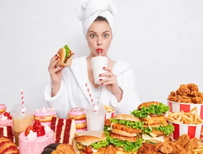 Mujer rodeada de hamburguesas, fritos, refrescos y dulces como ejemplo de la baja calidad alimentaria en España