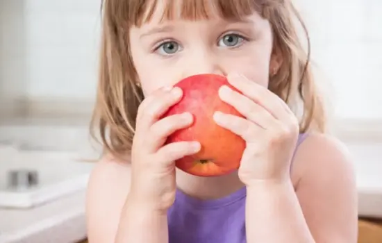 niña pequeña comiendo una manzana simbolizando alimentación saludable para niños