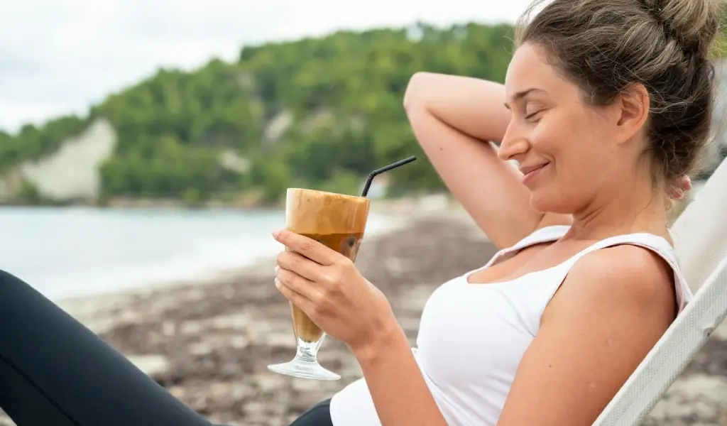Mujer disfrutando de una bebida en la playa durante el verano mientras cuida su alimentaci&oacute;n para no engordar en vacaciones