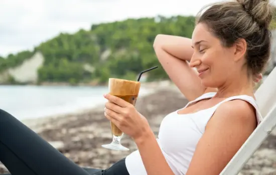 Mujer disfrutando de una bebida en la playa durante el verano mientras cuida su alimentación para no engordar en vacaciones
