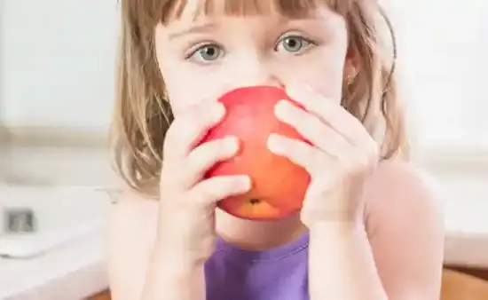 niña pequeña comiendo una manzana simbolizando alimentación saludable para niños