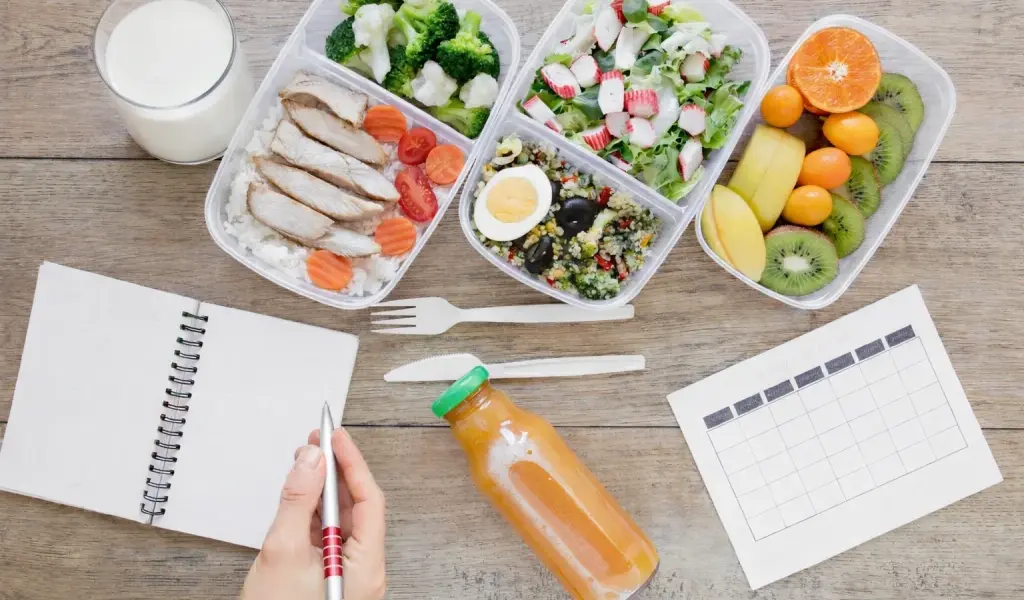 Planificaci&oacute;n semanal de meal prep con t&aacute;peres de pescado, verduras, fruta, huevo y vaso de leche