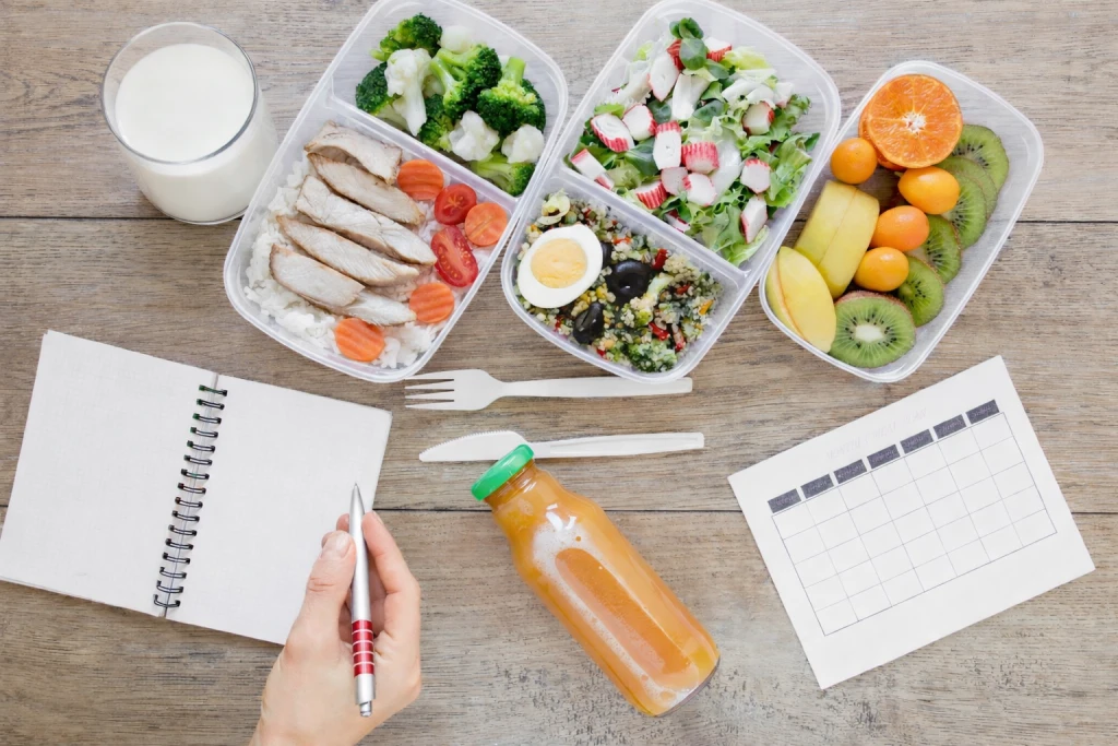 Planificaci&oacute;n semanal de meal prep con t&aacute;peres de pescado, verduras, fruta, huevo y vaso de leche