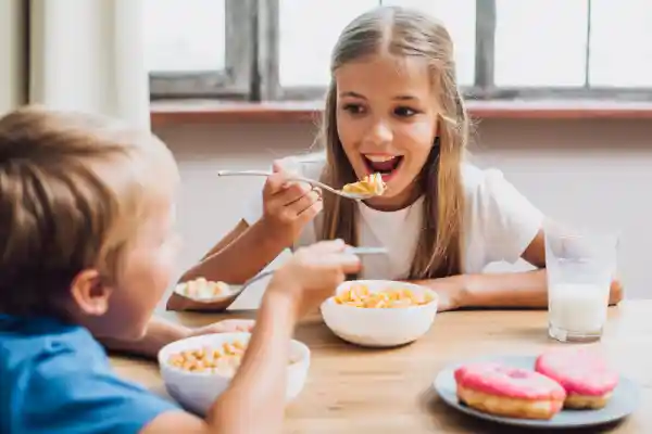 Alimentos que debes eliminar de la dieta de tu hijo: ultraprocesados comunes en una mesa (cereales azucarados, refresco, bollería, snacks)