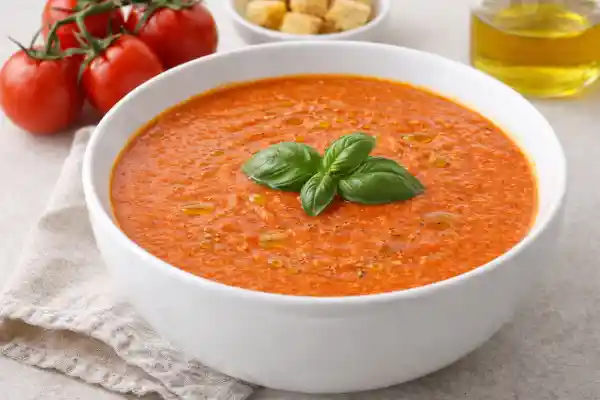 Crema de tomate casera servida en cuenco blanco con albahaca fresca y aceite de oliva