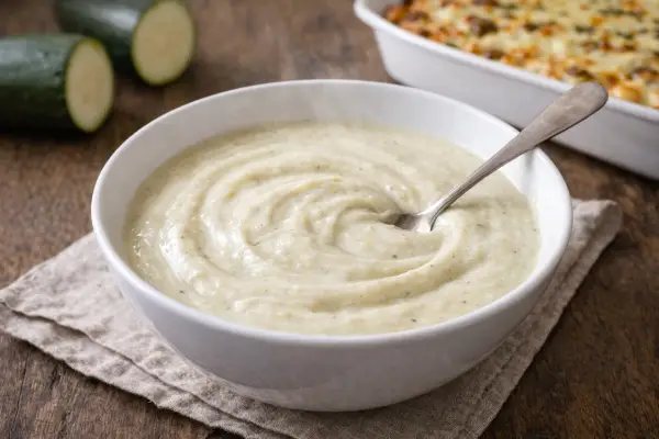 Bechamel baja en calor&iacute;as cremosa en cuenco blanco, salsa ligera tipo bechamel de calabac&iacute;n con luz natural