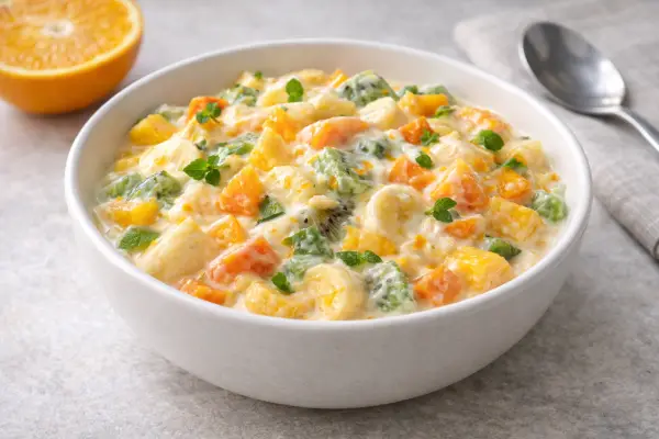 Macedonia de fruta con yogur a la naranja servida en bol, con mango, kiwi, pi&ntilde;a y frutos rojos, fotograf&iacute;a luminosa estilo gourmet sobre fondo neutro.