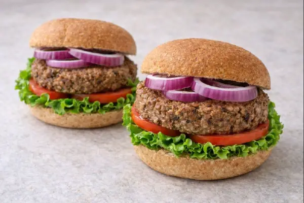 Hamburguesas de soja caseras servidas en pan integral con lechuga, tomate y cebolla morada, en fondo neutro y luz natural