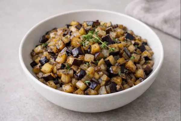 Guarnici&oacute;n de berenjenas salteadas con cebolla y tomillo, servida en cuenco blanco con luz natural y fondo neutro