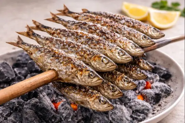 Espeto de sardinas a la brasa ensartado en ca&ntilde;a, con piel dorada y sal gorda, acompa&ntilde;ado de rodajas de lim&oacute;n; foto gourmet muy luminosa y fondo neutro.