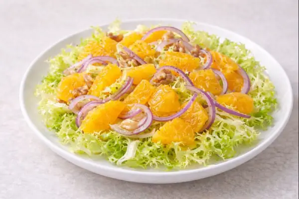 Ensalada de escarola y naranja servida en plato blanco, con escarola rizada, gajos de naranja y cebolla en l&aacute;minas finas, ali&ntilde;ada con aceite de oliva y vinagre de M&oacute;dena.