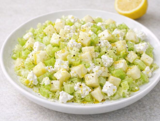 Ensalada de apio y manzana con dados de manzana, apio picado y queso fresco de cabra, aliñada con aceite de oliva y limón en plato blanco.