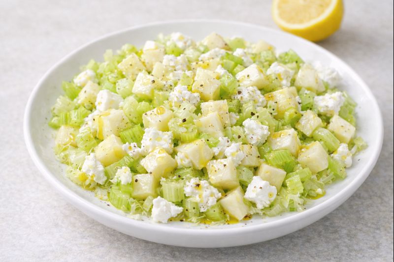 Ensalada de apio y manzana con dados de manzana, apio picado y queso fresco de cabra, ali&ntilde;ada con aceite de oliva y lim&oacute;n en plato blanco.