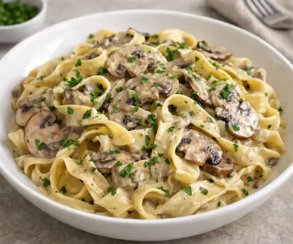 Cintas con salsa de setas cremosa, con setas salteadas y toque de perejil, servidas en plato blanco con fondo neutro.