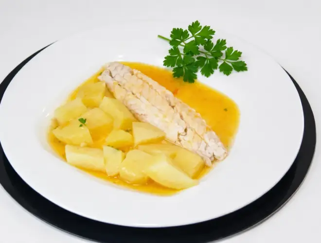 Lubina hervida con patatas y verduras cocidas, ali&ntilde;ada con aceite de oliva, en plato blanco con luz natural