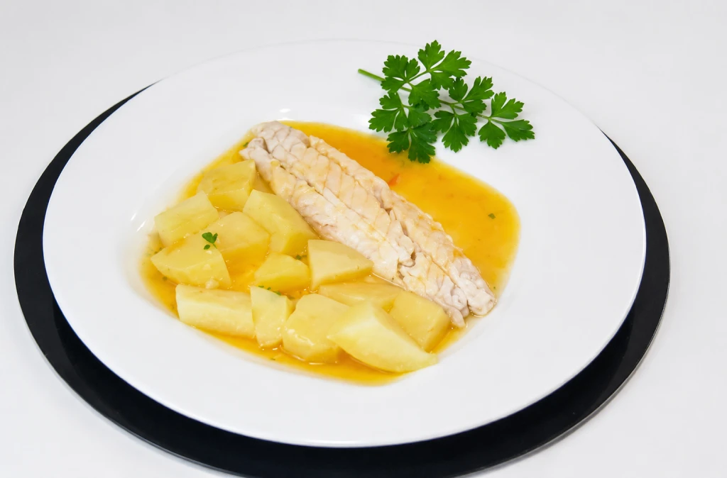 Lubina hervida con patatas y verduras cocidas, ali&ntilde;ada con aceite de oliva, en plato blanco con luz natural