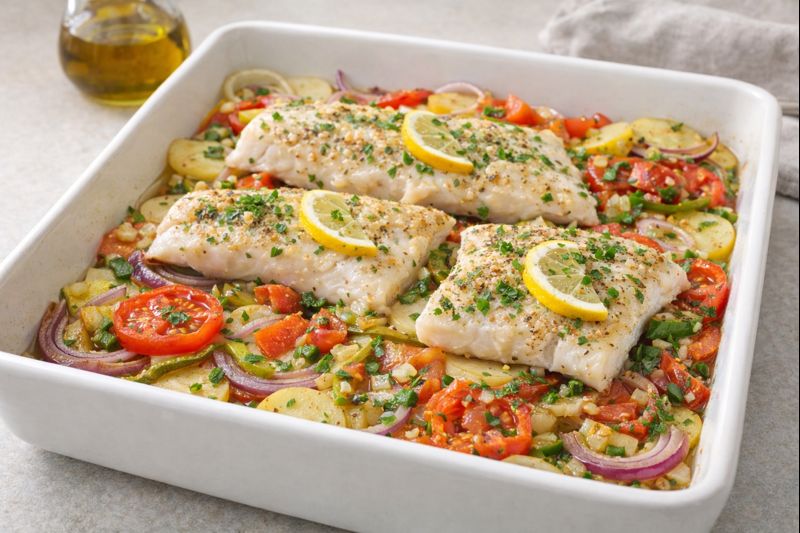 Pescado al horno sobre cama de patata, cebolla, pimiento rojo y verde y tomate, con majadillo de ajo, perejil, lim&oacute;n y aceite de oliva.