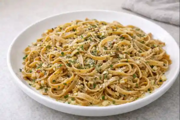 Pasta integral con ajo y especias salteada con ajo picado, aceite de oliva y queso rallado, servida en plato blanco con luz natural.