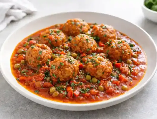 Alb&oacute;ndigas de soja en salsa con tomate y verduras servidas en plato blanco, acabado gourmet y luz natural.