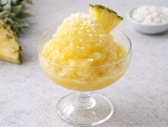 Sorbete de pi&ntilde;a y coco en copa de cristal, textura granizada y cremosa, con virutas de coco y gajo de pi&ntilde;a sobre fondo neutro luminoso