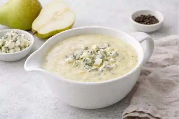 Salsa de peras cremosa en salsera blanca con dados de pera y roquefort desmigado, sobre fondo neutro y luminoso