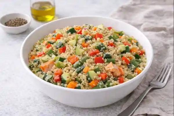 Quinoa con verdura en bol blanco con dados de calabac&iacute;n, zanahoria y pimiento rojo, presentada en fondo neutro y muy luminoso