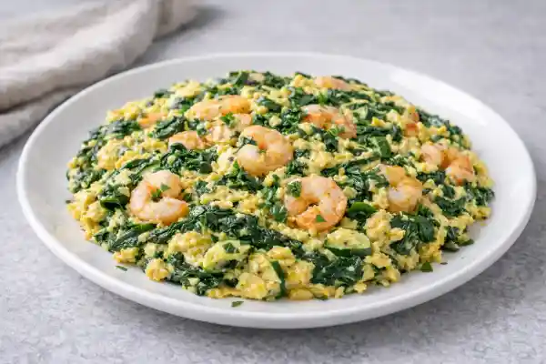 Revuelto de espinacas con gambas, jugoso y reci&eacute;n hecho, servido en plato blanco con luz natural y fondo neutro