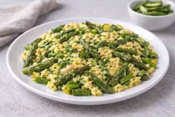 Revuelto de espárragos verdes y ajetes con huevo, servido en plato blanco con luz natural y fondo neutro