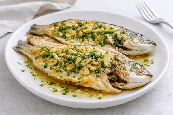 Dorada a la espalda a la plancha con piel dorada y crujiente, aceite de oliva, ajo en polvo y perejil sobre plato blanco, foto luminosa y realista