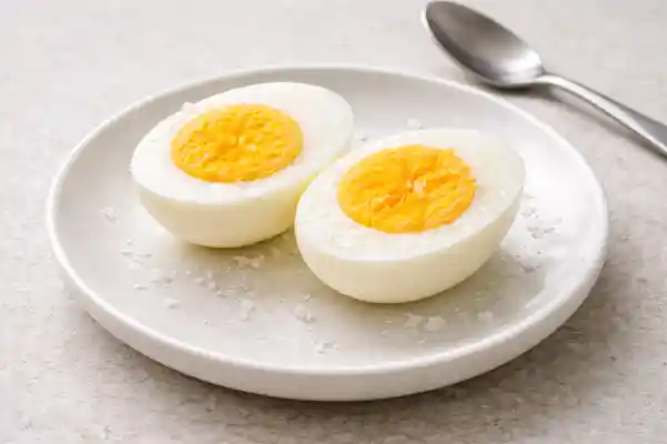 Huevo duro pelado y cortado por la mitad, con la yema cuajada, servido en plato blanco con fondo neutro.