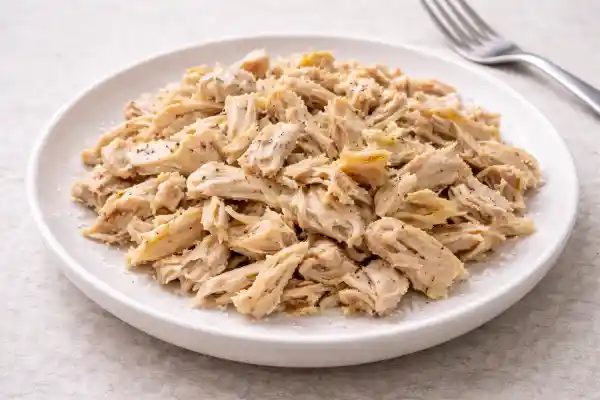 Contramuslo de pollo cocido desmigado en plato blanco, listo para usar en ensaladas y platos rápidos.