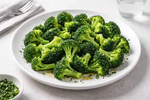 Brócoli al vapor en ramilletes verdes, aliñado con aceite de oliva y salpimentado, servido en plato blanco con luz natural y fondo neutro.