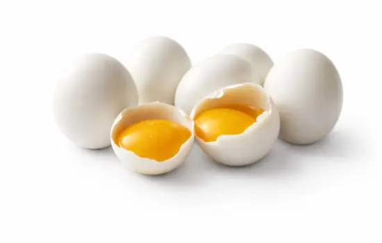 Huevos crudos con yema visible abiertos sobre fondo blanco