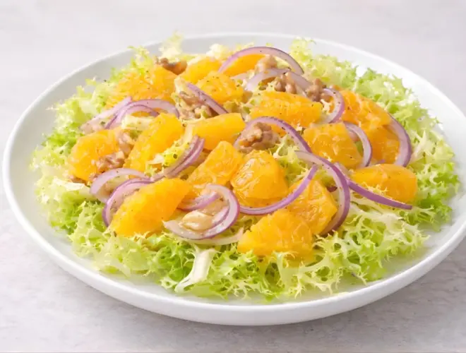 Ensalada de escarola y naranja servida en plato blanco, con escarola rizada, gajos de naranja y cebolla en l&aacute;minas finas, ali&ntilde;ada con aceite de oliva y vinagre de M&oacute;dena.