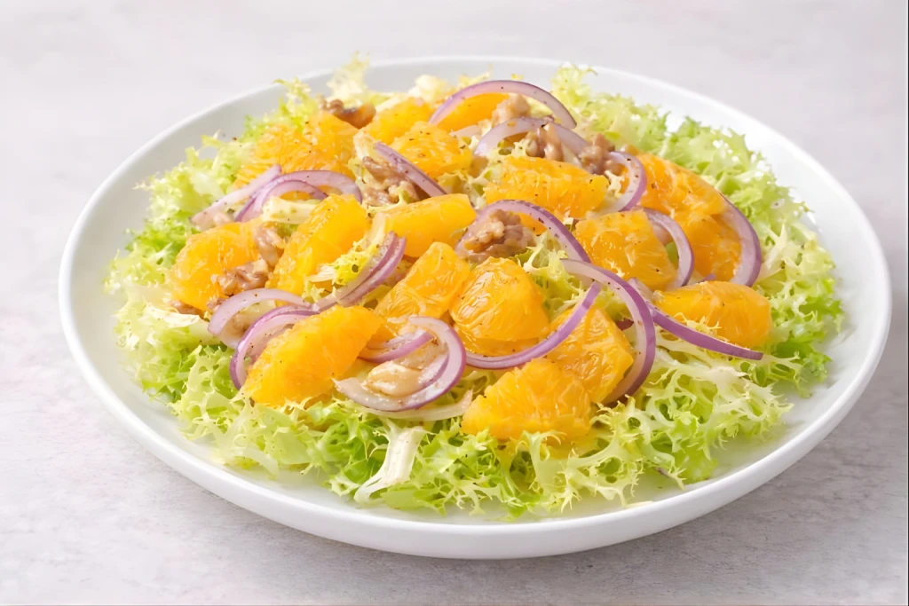 Ensalada de escarola y naranja servida en plato blanco, con escarola rizada, gajos de naranja y cebolla en l&aacute;minas finas, ali&ntilde;ada con aceite de oliva y vinagre de M&oacute;dena.