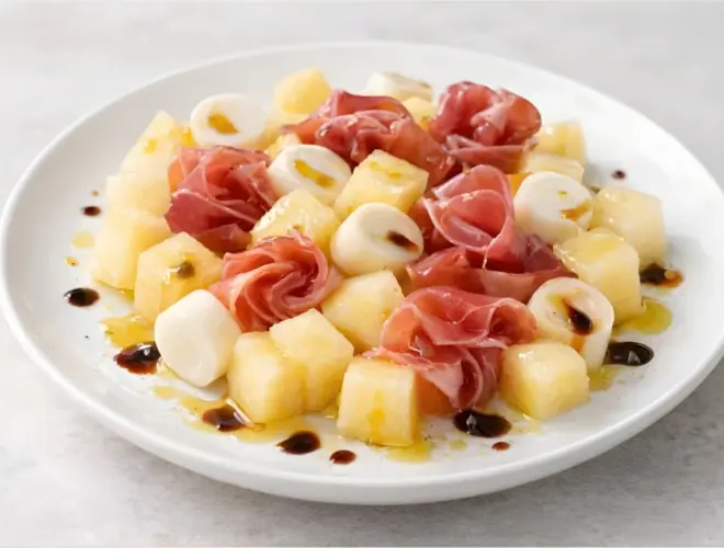 Ensalada de mel&oacute;n, palmito y jam&oacute;n serrano en plato blanco, con dados de mel&oacute;n, rodajas de palmito y jam&oacute;n, ali&ntilde;ada con aceite de oliva y vinagre de M&oacute;dena.