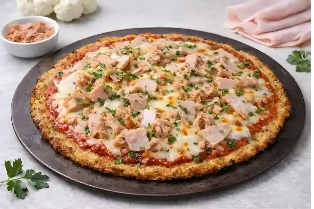 Pizza con base de coliflor de at&uacute;n y pavo, con queso fundido, salsa de tomate y base crujiente de coliflor.