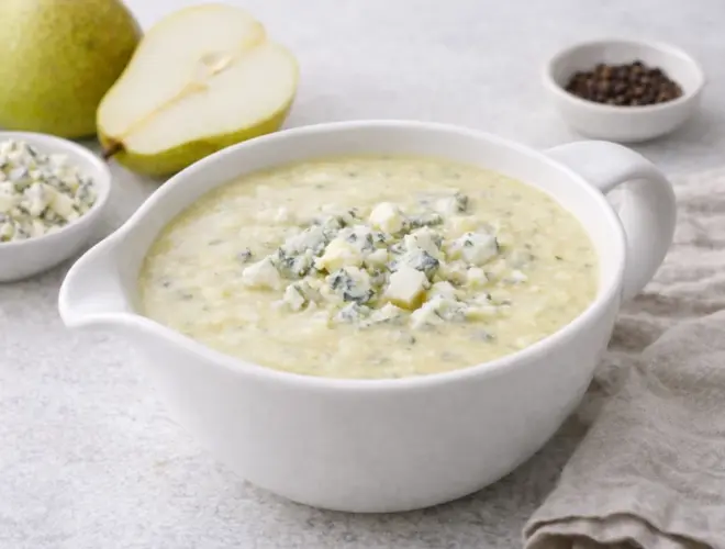 Salsa de peras cremosa en salsera blanca con dados de pera y roquefort desmigado, sobre fondo neutro y luminoso