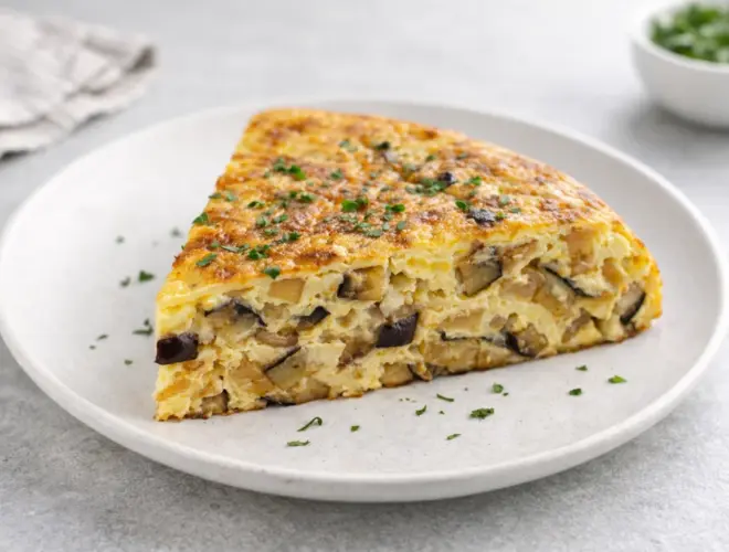 Tortilla de berenjenas jugosa con dados de berenjena y cebolla, servida en plato blanco con luz natural y fondo neutro