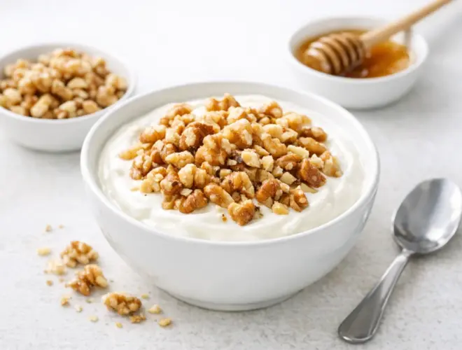 Yogur con nueces en cuenco blanco, cremoso y luminoso, con nueces troceadas por encima y fondo neutro.
