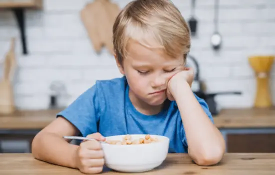 Niño pequeño mostrando rechazo a la comida sentado frente a un bol durante la hora de comer
