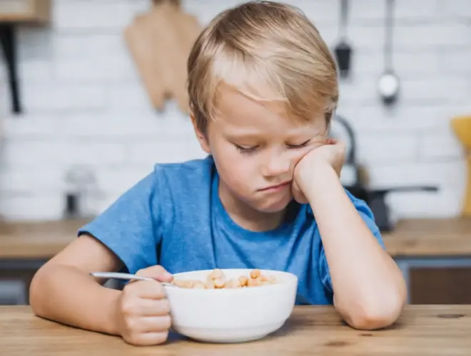 Niño pequeño mostrando rechazo a la comida sentado frente a un bol durante la hora de comer