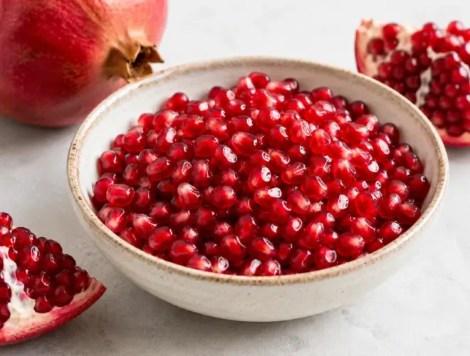 Granada abierta con granos rojos servidos en un bol de cer&aacute;mica sobre fondo neutro, fotograf&iacute;a luminosa y realista de fruta fresca.