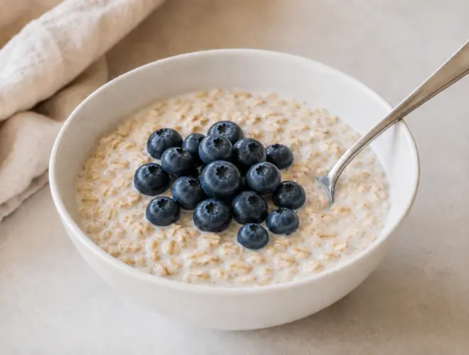 Porridge de avena con leche sin lactosa en cuenco blanco, fotograf&iacute;a gourmet luminosa con topping m&iacute;nimo y fondo neutro.