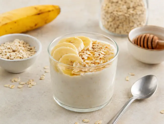 Yogur sin lactosa con pl&aacute;tano y avena en bol blanco, textura cremosa y copos visibles, fondo neutro luminoso